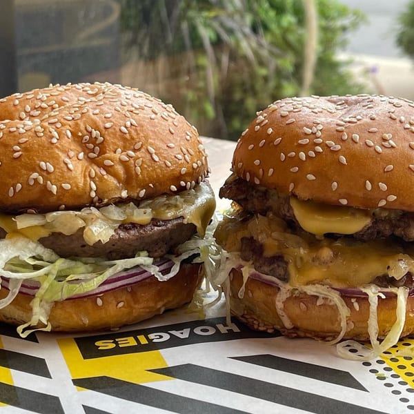 Two Taylor Gourmet burgers with melted cheese, lettuce, onions, and sesame seed buns.