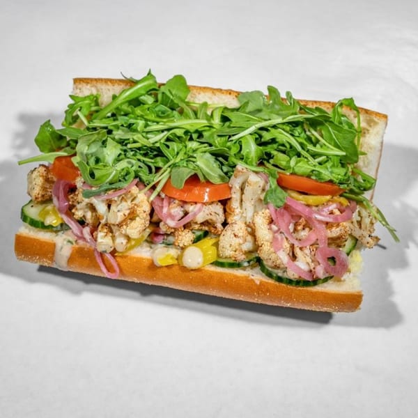 Taylor Gourmet sandwich with roasted cauliflower, pickled onions, tomatoes, cucumbers, and arugula on a baguette.
