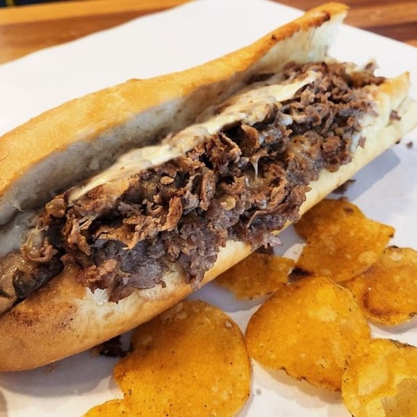 Taylor Gourmet cheesesteak sandwich with melted cheese and steak, served with crispy chips.