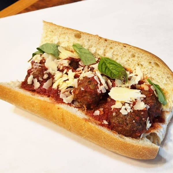 Taylor Gourmet's meatball sub with marinara, shredded cheese, and fresh basil on a white background.