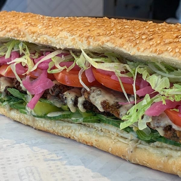 Taylor Gourmet sandwich with falafel, lettuce, tomatoes, pickled onions, and sauce on a sesame seed roll.