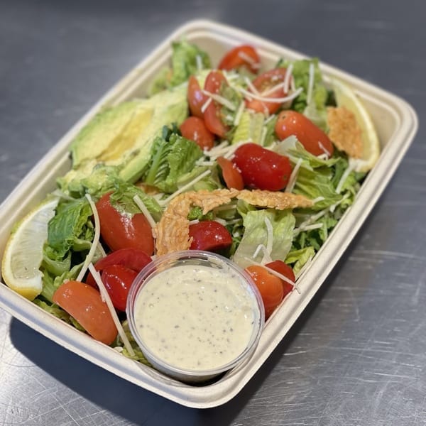 Taylor Gourmet salad with lettuce, cherry tomatoes, avocado, cheese, lemon, and dressing.