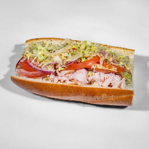 A Taylor Gourmet sandwich, cut in half, filled with turkey, tomatoes, red onions, and shredded lettuce.