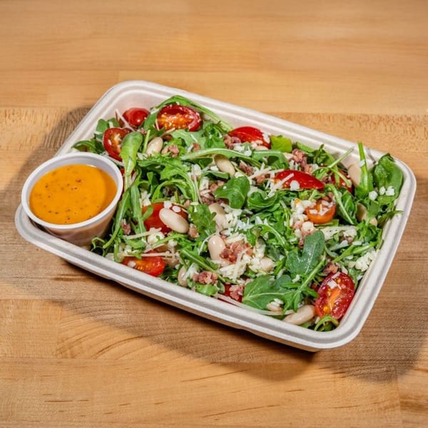 Taylor Gourmet salad with arugula, tomatoes, white beans, cheese, and bacon bits, with dressing on the side.